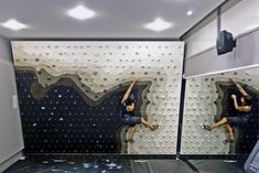 two people climbing up the side of a wall in front of a mirror with rocks on it