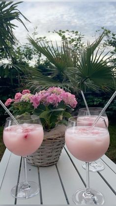 two glasses filled with pink liquid sitting on top of a wooden table next to flowers