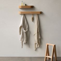 two coats hanging on the wall next to a wooden stool and shelf with an umbrella