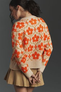 a woman is wearing an orange and white sweater with flowers on the back, while she has her hands in her pockets