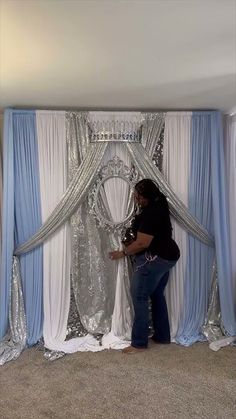 a woman standing in front of a white and blue backdrop with silver sequins