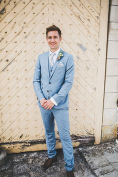 a man wearing a blue suit and tie standing in front of a wooden door