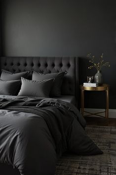 a bed with black linens and pillows in a dark room next to a window