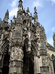 an old cathedral with statues on the front and side walls, against a blue sky