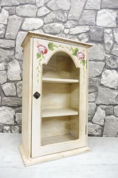 an old wooden cabinet with painted flowers on the front and bottom, next to a stone wall