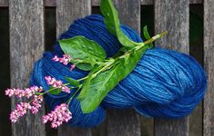 a skein of blue yarn with green leaves and pink flowers on the end, sitting on a wooden bench