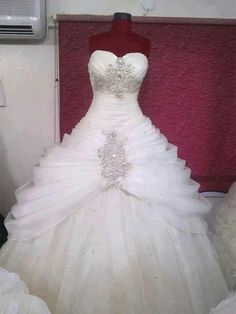 a wedding dress is displayed on a mannequin in front of a red wall