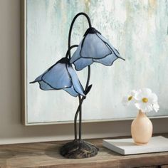 two blue stained glass flowers on a table next to a vase with white flowers in it