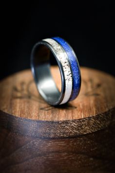 two wedding bands with silver and blue inlays on top of a wooden stand