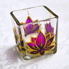 a small glass candle holder with purple and yellow designs on it's sides, sitting on a white surface