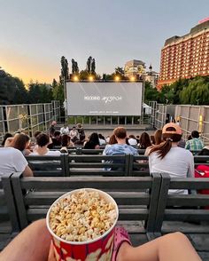 people sitting on benches watching a movie at an outdoor cinema in front of a large screen