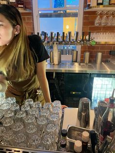 a woman standing behind a bar filled with glasses