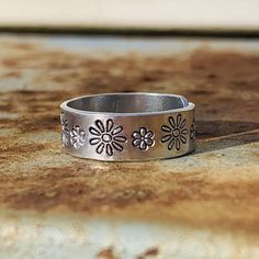 If you love flowers and/or being outdoors, this ring is perfect for you! Daisy flowers in two sizes adorn this hand crafted adjustable (midi) ring. I personally hand stamp all of the lettering and designs in my studio. Each design is hand aligned and punched into the metal, so the placement of the wording and designs will vary slightly from piece to piece. After stamping, I darken the impressions so they stand out. To retain the contrast, it is highly recommended that the piece is not exposed to Personalized Silver Adjustable Flower Ring, Flower Shaped Engraved Adjustable Promise Ring, Bohemian Style Engraved Ring As Gift, Adjustable Flower Engraved Promise Ring, Adjustable Hand Stamped Midi Rings, Adjustable Hypoallergenic Flower Promise Ring, Adjustable Vintage Stackable Rings For Gift, Unique Adjustable Flower Promise Ring, Bohemian Adjustable Flower Ring For Anniversary