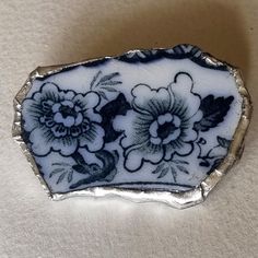 a white and black flowered brooch sitting on top of a table next to a wall