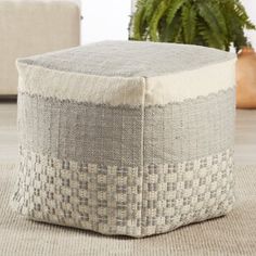 a large square ottoman sitting on top of a rug next to a potted plant