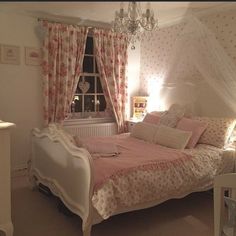 a white bed sitting under a window next to a chandelier in a bedroom