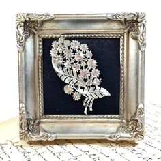 an ornate silver frame with flowers and leaves in it on top of a white table