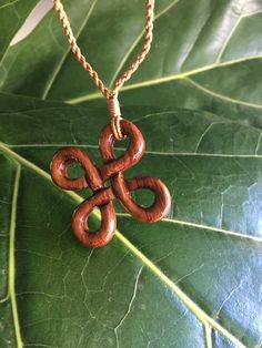 a wooden necklace with an intricate knot on it's end sitting on a green leaf