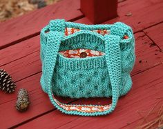 a knitted purse sitting on top of a wooden bench next to a pine cone