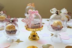 three small cakes in glass cases on a table with confetti and paper decorations