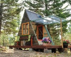 a tiny cabin in the woods with lots of windows and plants on the porch area