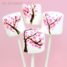 four marshmallows decorated with cherry blossoms on a pink background