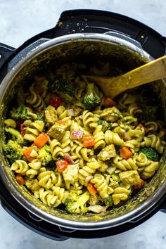 a pot full of pasta and vegetables with a wooden spoon in the top left corner