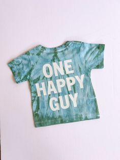 "Celebrate your little one's big milestone with a touch of retro charm with our \"One Happy Guy\" first birthday shirt for baby boys. This tie-dye shirt is the perfect blend of fun and style for your little man's special day. Featuring a vibrant color palette and a playful retro theme, this 1st birthday boy shirt is sure to stand out in all the birthday photos and create lasting memories. Made for comfort and cuteness, this one-year-old boy shirt is a must-have birthday outfit for your little gu Playful Green T-shirt For Birthday, Blue Short Sleeve T-shirt For First Birthday, Blue Summer T-shirt For First Birthday, Blue Cotton T-shirt For First Birthday, Blue Short Sleeve Tops For Birthday Gift, Cute T-shirt For First Birthday And Father's Day, Cute T-shirt For First Birthday On Father's Day, Father's Day Playtime T-shirt With Short Sleeves, Father's Day Short Sleeve Playtime T-shirt