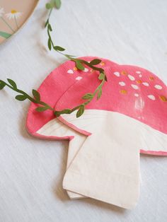 a pink hat with white flowers and green leaves on it sitting on top of a table