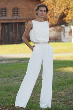 a woman standing in the grass with her hands on her hips wearing a white jumpsuit