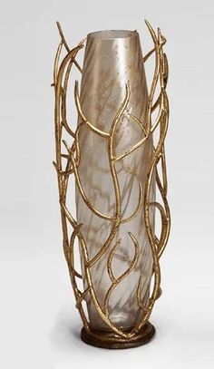 a glass vase with gold branches on the top and bottom, sitting in front of a white background