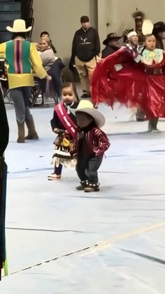 two young children in costumes are dancing on the stage with other people watching from behind them