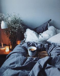 a bed with blue sheets and pillows next to a vase filled with baby's breath flowers