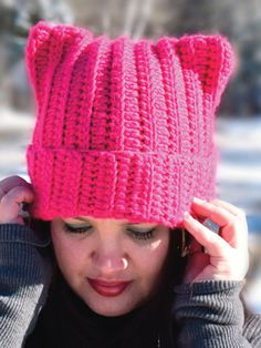 a woman wearing a pink knitted hat with ears on top of her head, in the snow