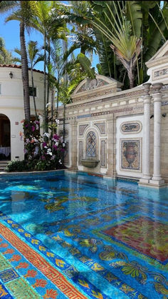 an outdoor swimming pool surrounded by palm trees and colorful tile work on the floor, along with potted plants