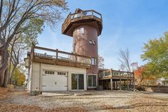 a large brown tower house sitting on top of a dirt field next to trees and leaves