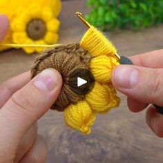 a person holding a tiny yellow flower in their left hand and knitting it on the needle