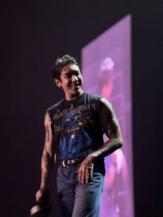 a man with tattoos on his arms and chest standing in front of a purple light