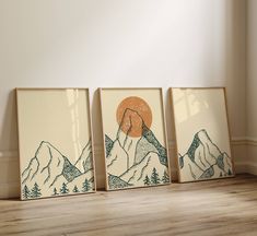 three framed art pieces on the floor in front of a wall with mountains and trees