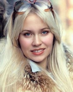 a woman with long blonde hair wearing sunglasses and a fur coat on her head is smiling at the camera