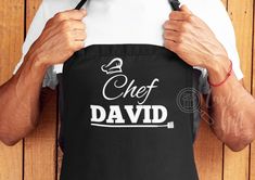 a man holding an apron with the words chef david printed on it