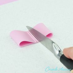 someone cutting paper with a pair of scissors on top of it and another piece of pink paper in the background