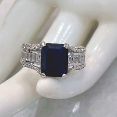 There Are No Words To Describe This Exquisitely Stunning Magnificently Cut Kanchanaburi Blue Sapphire Ring Featuring A Bridge Design That Elevates And Gives Grandeur To The Center Stone. The Band Is Accented With White Topaz Baguettes On The Face And White Topaz Stones On The Sides Set In Sterling Silver Marked 925 Size 8 Dazzling Sapphire Rings Emerald Cut, Blue Gia Certified Emerald Ring For Formal Occasions, Dazzling Emerald Cut Sapphire Rings, Timeless Blue Radiant Cut Sapphire Ring, Blue Cubic Zirconia Sapphire Ring Channel Set, Octagon Sapphire Ring With Accent Stones, Blue Sapphire Ring With Cubic Zirconia Channel Set, Blue Sapphire Ring With Channel Set Cubic Zirconia, Blue Sapphire Ring With Radiant Cut And Accent Stones