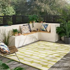 an outdoor area with plants and pillows on the bench, along with a green rug