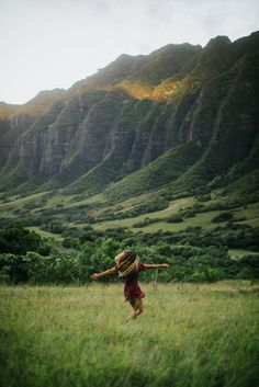 a woman is running through the grass with mountains in the backgrouds behind her