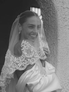 a woman in a wedding dress and veil smiles at the camera while standing next to a wall