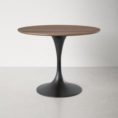 an oval wooden table with black metal base on a white floor, against a plain wall