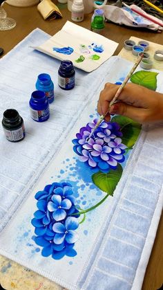 a person is painting flowers on a piece of cloth with watercolors and paint