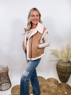 Camel Tan Suede Vest with Sherpa Trim Upgrade your winter wardrobe with our Camel Tan Suede Vest with Sherpa Trim. This chic vest is perfect for a stylish snow day outfit, offering a luxurious look and feel that will make you stand out. The soft suede material in a rich camel tan color is complemented by plush fur trim at the edges, giving it a high-end, sophisticated vibe. With a zipper front and side pockets, this vest combines practicality with elegance. The relaxed fit ensures comfort, makin Beige Winter Vest For Cold Weather, Beige Vest For Winter Cold Weather, Beige Vest For Cold Weather In Winter, Beige Vest For Cold Weather And Winter, Beige Winter Vest Outerwear, Winter Beige Sleeveless Outerwear, Brown Sleeveless Vest For Cold Weather, Beige Vest For Cold Weather In Fall, Brown Winter Vest Outerwear