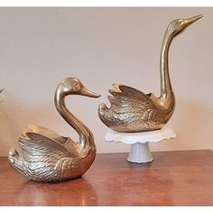 two brass swan figurines sitting on top of a cake plate